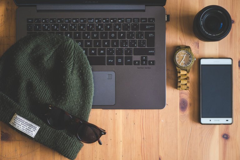 A laptop and iPhone with a beanie and sunglasses laid on top