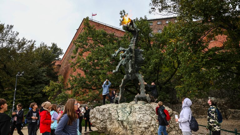 People gather around a tall bonze sculpture of a dragon that emits actual fire