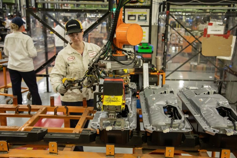 a factory worker works on factory link assembling a car engine